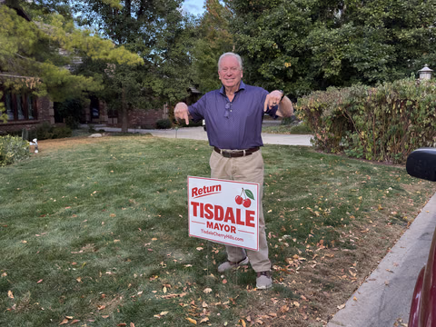 A supporter standing behind a Doug Tisdale sign beside a lawn.