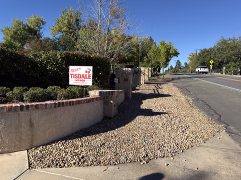 A Doug Tisdale sign above a stone wall beside a road.